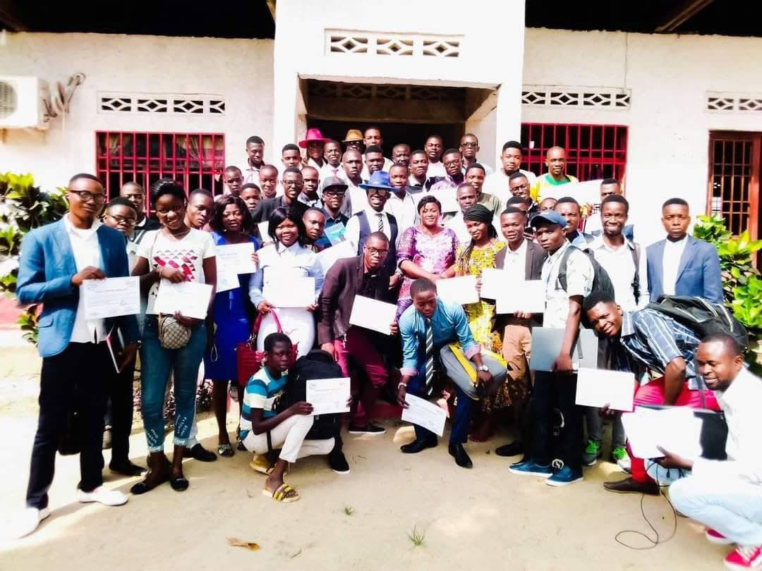 Participants posing together with certificates in front of a building.